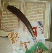 Zdjęcie przedstawiające m.in. gęsie pióro i kilka wykonanych w czasie zajęć iluminowanych złotem i srebrem inicjałów.