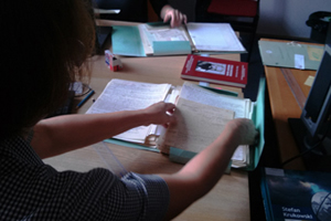 Zdjęcie, na którym widać osobę pracującą przy układaniu archiwaliów - rękopisów prac naukowych i notatek wielkich archeologów.